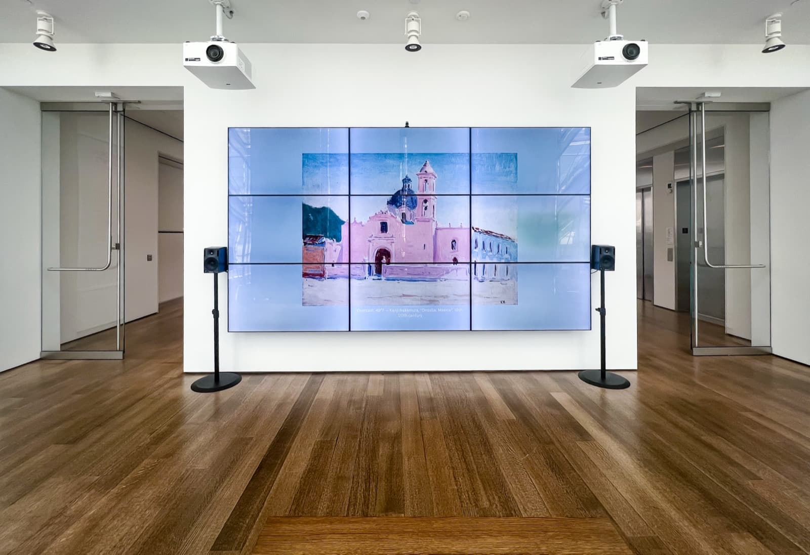 An installation shot of a Harvart Art Museum gallery with a large screen on the wall. The screen shows a picture of a painting from the museum's digital collection on a blurred background of the sky. The image is captioned with the current weather (Overcast, 45°F) and the artwork's title and artist